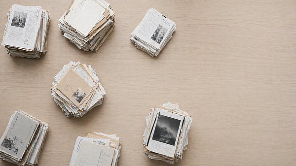[Translate to English:] Mehrere voneinander getrennte Stapel aus Papierdokumenten auf einem großen hellen Holztisch von oben fotografiert.