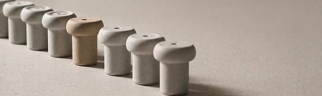 [Translate to English:] Reihe identischer heller Keramik-Objekte im Studiolicht, bei der ein einzelnes Stück leicht nach vorne versetzt und wärmer getönt ist.