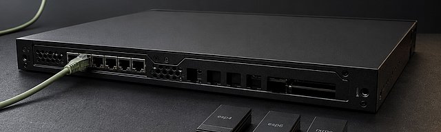 A matte-black server-edge appliance with one sage-green patch cable to an active port; on the slate surface beside it, three separated module cartridges with mono-labels esp4, esp6, rxrpc — metaphor for deliberately blacklisted kernel modules as a mitigation, cool studio light.