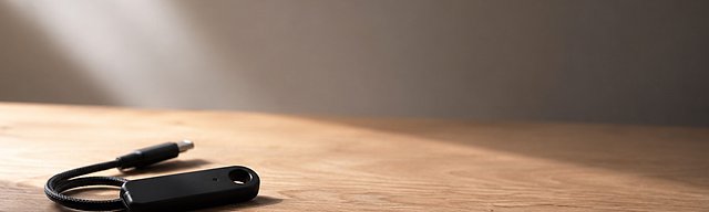 [Translate to English:] Mattschwarzes Hardware-Security-Token mit gewickeltem USB-C-Kabel auf einer Eichenholz-Oberfläche, weiches Tageslicht von links — Metapher für die Permissions- und Identitäts-Boundary, die Project Arc und OpenShell für autonome Agenten schaffen.