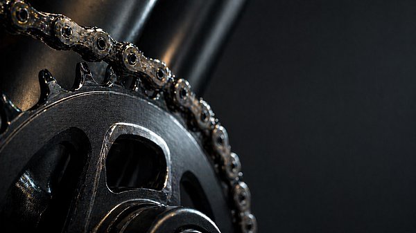 Nahaufnahme einer frisch geölten Fahrradkette und Kettenblatt mit scharfen Details im Studiolicht.
