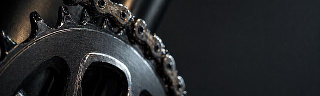 [Translate to English:] Nahaufnahme einer frisch geölten Fahrradkette und Kettenblatt mit scharfen Details im Studiolicht.