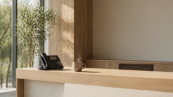 Aufgeräumter moderner Empfangstresen mit Telefon und Kaffeetasse im hellen Tageslicht.