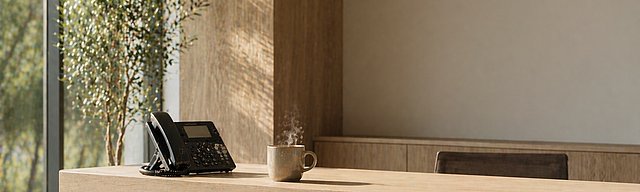 [Translate to English:] Aufgeräumter moderner Empfangstresen mit Telefon und Kaffeetasse im hellen Tageslicht.