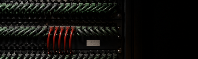 Dense server rack in dark tones with a uniform grid of forest-green patch cables; a single oxblood-red cable bundle crosses the grid as a visual anomaly — metaphor for hidden logic in obfuscated code.