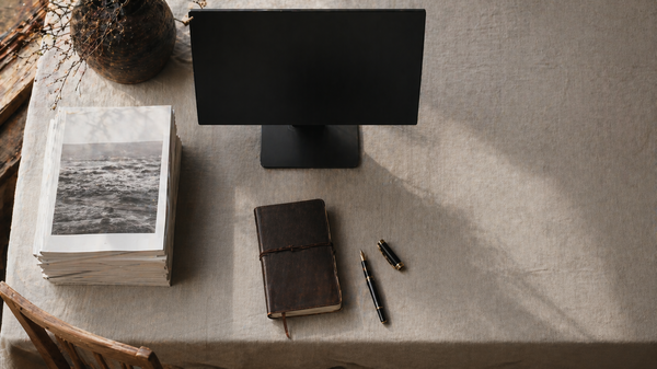 [Translate to English:] Aufgeräumter Redaktions-Arbeitsplatz von oben mit gestapelten gedruckten Magazinen neben einem ausgeschalteten Monitor.